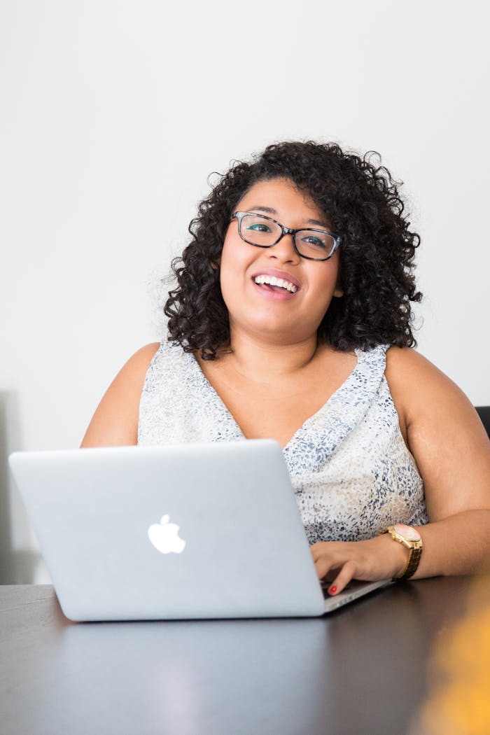Happy businesswoman with curly hair using a laptop at her desk, smiling confidently.